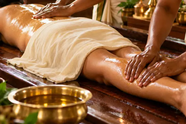 Two therapists applying warm herbal oil during an Abhyanga massage session in Kovalam